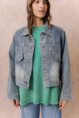 Campera de denim con lavado claro y efecto desgastado. Presenta cuello camisero, cierre frontal con botones metálicos, dos bolsillos frontales con tapa y botón, y puños abotonados.