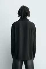 Camisa de corte relajado confeccionada en una mezcla de viscosa y algodón con textura. Presenta cuello solapa, cierre frontal de botones, manga larga con puños abotonados y aberturas laterales en el bajo.