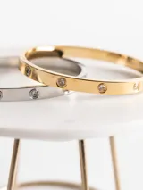 Pulsera rígida dorada con circonitas incrustadas, hecha de acero quirúrgico con baño de oro de 18k.