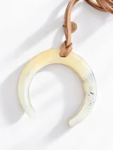 Collar con dije de herradura de resina marmolada en tonos beige y translúcido, suspendido de un cordón de cuero sintético tostado con detalle de placa metálica con grabado.