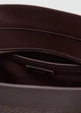 Bolso tipo shopper de tamaño mediano confeccionado en tejido de fibra natural con detalles en poliuretano. Cuenta con dos asas largas para llevar al hombro, cierre de cremallera superior, bolsillo interior y un charm colgante decorativo con herrajes dorados.