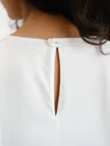 Vestido midi blanco sin mangas, con cuello redondo y diseño holgado. Presenta un cordón ajustable fruncido en el centro de la parte frontal y parches circulares sutiles en la tela.