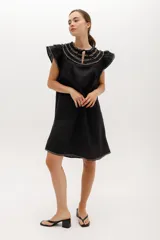 Vestido negro de lino, corte suelto, con cuello redondo con volados y mangas cortas con volados.
