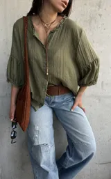 Camisa verde de tejido liviano, con cuello romántico con volados, mangas abullonadas tres cuartos con puños fruncidos y cierre frontal con botones.