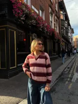 Sweater tejido de punto con diseño de rayas horizontales anchas en tonos rosado y bordó, corte holgado, mangas largas y cuello tipo polo con escote en V.