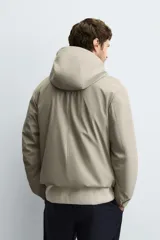 Parka de tejido técnico con acabado engomado, cuello subido y capucha ajustable. Presenta cierre frontal con cremallera oculta bajo solapa con botones a presión, bolsillos laterales de vivo y mangas largas con puños ajustables.