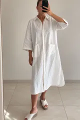 Vestido midi blanco de lino, con cuello camisero, cierre frontal con botones ocultos, bolsillos plaqué en el pecho con costuras en contraste y mangas tres cuartos.