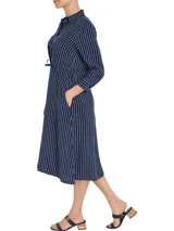 Vestido camisero midi azul marino con rayas verticales blancas, cuello camisero, cierre frontal con botones, mangas largas con puños abotonados y cinturón de lazo a juego.