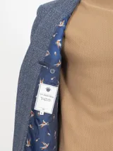 Saco de paño marrón con diseño a cuadros en tonos marrón, rojo y blanco. Tiene cuello con solapas, bolsillos de plastrón en pecho y cadera, mangas con coderas en contraste de color, forro estampado y aberturas en espalda.