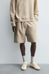 Bermuda de algodón color beige, estilo jogger, con corte relajado, cintura elástica ajustable con cordón y bolsillos laterales y trasero.