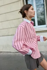 Camisa oversize de popelina rosa con rayas verticales marrones, cuello solapa blanco y escote en pico. Mangas largas con puños anchos blancos a contraste y cierre frontal con botones.