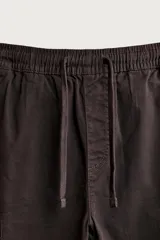 Pantalón cargo de corte ajustado en color negro, confeccionado en tejido de algodón con elasticidad. Presenta cintura elástica con cordón ajustable, bolsillos laterales tipo cargo con solapa y bajo con puños elásticos.