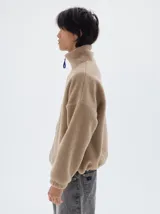 Campera de sherpa color beige con cuello alto, cierre frontal a contratono en color azul y bordado de la marca Pastiche en el pecho.