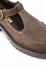 Zapato tipo guillermina de cuero lavado color marrón, con diseño de tira en T y cierre de hebilla metálica. Presenta costuras decorativas en contraste y suela de goma con plataforma dentada.