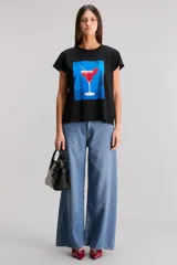 Remera negra de jersey de algodón, con cuello redondo, manga corta y estampado frontal de un cóctel rojo en un vaso de martini sobre un fondo azul.