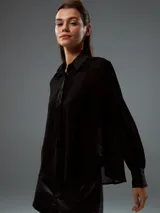 Camisa de tela semitransparente color negro, con cuello clásico, cierre frontal de botones y mangas largas con puños ajustados.