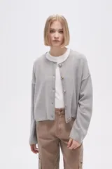Cardigan de tejido de punto gris, con cuello redondo, cierre frontal con botones y mangas largas de corte holgado.