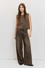 Pantalón de denim estilo wide leg color marrón gastado, con apliques de tachas metálicas o strass distribuidos por toda la prenda y tiro medio.