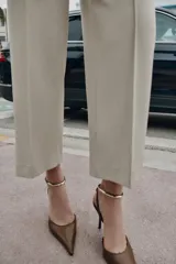 Zapato de tacón destalonado con acabado en punta y escote redondo. Presenta una pulsera al tobillo con hebilla ajustable y un detalle metálico decorativo. Cuenta con tacón alto fino.