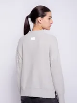 Suéter gris de punto con cuello alto, mangas largas y anchas, detalle de línea vertical rosa contrastante en las mangas y aberturas laterales.