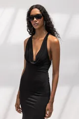 Vestido largo negro de corte al cuerpo, con escote halter y cuello drapeado. Presenta una silueta entallada que se ensancha suavemente hacia el ruedo.