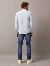 Camisa celeste de algodón orgánico, corte slim fit, con cierre frontal de botones, bolsillo de parche en el pecho y logo de Calvin Klein en el lateral.