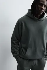 Sudadera tipo hoodie de color blanco hueso, con capucha, manga larga y bolsillo canguro frontal. Presenta un calce relajado y tejido de algodón con interior afelpado.