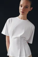 Camiseta de algodón con cuello redondo y manga corta. Presenta un diseño entallado con pinzas en la cintura y bajo recto.