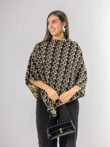Poncho liviano con diseño geométrico de letras entrelazadas en color negro y beige. Presenta un corte asimétrico y caída fluida, ideal para superponer sobre otras prendas.