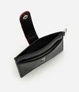 Billetera compacta Satinato de poliuretano color negro, con solapa frontal con botón a presión, detalles en rojo y argolla lateral metálica.
