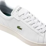 Championes Lacoste modelo Carnaby Pro, de diseño clásico y minimalista en color blanco. Presentan el icónico logo del cocodrilo bordado en el lateral, con detalles en color azul oscuro en el talón y suela de goma al tono.