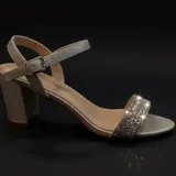 Sandalia de tacón cuadrado con acabado brillante plateado. Presenta una tira frontal decorada con pedrería brillante y una tira ajustable con hebilla en el tobillo.