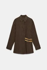 Camisa de cuello solapa y manga larga, color marrón con rayas verticales blancas. Presenta cierre frontal con botones ocultos y dos hebillas decorativas en color beige en el lateral.