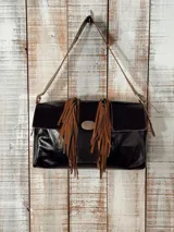 Bolso tipo bandolera de gamuza color marrón, con diseño de flecos frontales y detalle de hebilla metálica central. Cuenta con correa larga ajustable para llevar al hombro.
