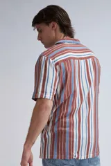 Camisa de manga corta con cuello solapa y cierre frontal con botones. Presenta un estampado de rayas verticales en tonos marrón, azul y blanco.