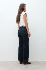 Pantalón de jean oscuro de tiro alto, corte recto y pierna ancha, con costuras verticales marcadas en el frente.