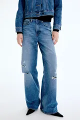 Jean de tiro alto con corte wide leg y diseño de cinco bolsillos. Presenta un acabado en denim azul con detalles de roturas desgastadas en la parte frontal.