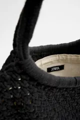 Bolso tipo shopper color crudo, confeccionado en tejido trenzado de algodón con diseño de macramé. Cuenta con dos asas de hombro ajustables que funcionan como cierre del compartimento principal.