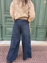 Pantalón tipo jean cargo de corte ancho y tiro alto, confeccionado en denim azul oscuro. Presenta bolsillos laterales tipo cargo con solapa y costuras reforzadas a lo largo de las piernas.