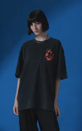 Remera de manga corta con cuello redondo y calce oversize, color negro con efecto nevado. Presenta una estampa frontal en color naranja con diseño gráfico de un rostro rodeado de llamas y texto tipográfico.