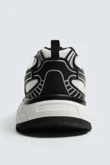Zapatilla deportiva tipo running con diseño de paneles superpuestos en combinación de materiales. Presenta cordonera curvada y suela con volumen de diseño irregular.