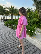 Vestido corto color beige de lino, con cuello mao, mangas cortas con volados, tablas en el canesú y falda escalonada con volantes.