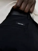 Pantalón chino de sarga elástica, color negro, de corte slim y talle medio. Incluye cinturón con hebilla en forma de D.