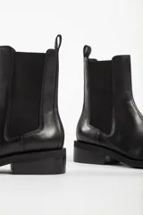 Bota tipo Chelsea de cuero color beige, con paneles laterales elásticos en color negro, puntera cuadrada y suela de goma negra con tacón bajo.