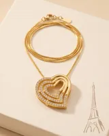 Collar de acero con baño de oro y delicada cadena fina, con un dije colgante en forma de corazón en relieve adornado con incrustaciones de circonias brilhantes.