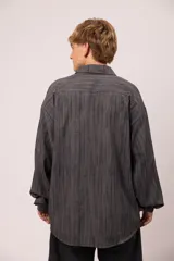 Camisa de manga larga con corte relajado, confeccionada en microfibra con estampado abstracto de líneas verticales en tonos grises. Presenta cuello clásico, cierre frontal con botones, bolsillo en el pecho con el nombre de la marca bordado.
