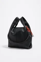 Bolso de mano mediano Bimba y Lola modelo Paper, confeccionado en piel vacuna negra, de estructura blanda y forma trapezoidal. Posee asas de mano y un cordón decorativo naranja y blanco en uno de los laterales. Lleva el logo metálico de la marca en la parte inferior frontal.