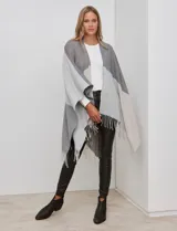 Ruana tejida con diseño colorblock en tonos de gris y beige, con flecos en el borde inferior.
