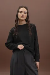 Sweater de punto color negro, de corte holgado y manga larga, con detalle de bordado calado en los hombros y a lo largo de las mangas.
