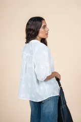 Blusa de algodón color blanco con bordado sutil en relieve, cuello redondo, cierre frontal con botones y mangas tres cuartos con terminación elástica.